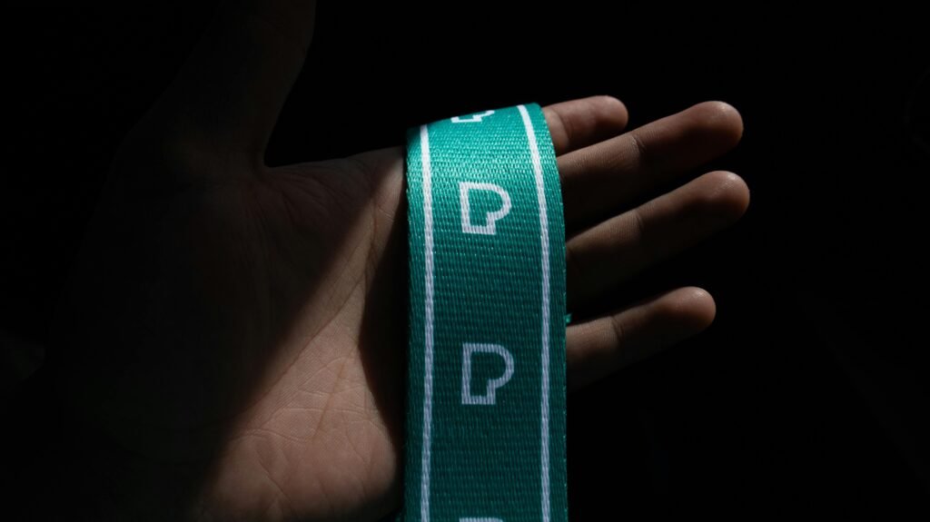Hand holding a green lanyard with 'P' letters, dramatic lighting.